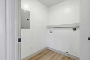 Laundry area featuring electric panel, light wood-type flooring, and washer hookup