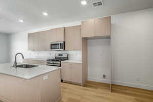 Kitchen featuring light wood finished floors, appliances with stainless steel finishes, modern cabinets, light stone countertops, and light brown cabinets