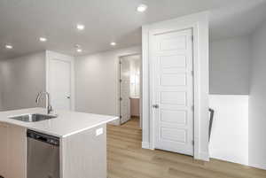 Kitchen featuring dishwasher, light wood-style floors, a kitchen island with sink, recessed lighting, and light stone countertops