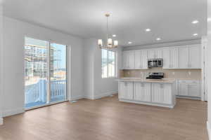 Kitchen with white cabinets, stainless steel appliances, a kitchen island with sink, hanging lights, and light wood-style flooring
