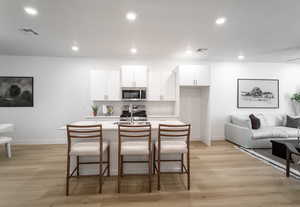 Kitchen featuring white cabinetry, a kitchen breakfast bar, light wood-type flooring, recessed lighting, and stainless steel appliances