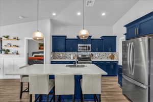 Kitchen featuring blue cabinets, a breakfast bar area, stainless steel appliances, an island with sink, and light wood-style floors