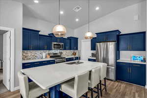 Kitchen featuring blue cabinetry, a kitchen bar, stainless steel appliances, a kitchen island with sink, and high vaulted ceiling