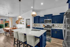 Kitchen with blue cabinetry, stainless steel appliances, decorative light fixtures, a breakfast bar, and a center island with sink