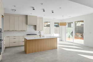 Kitchen featuring cream cabinets, a center island with sink, hanging light fixtures, light stone countertops, and double oven