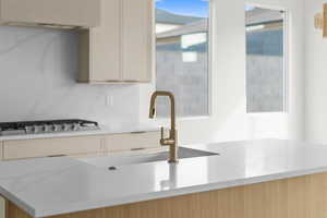 Kitchen with light stone counters, stainless steel gas cooktop, and cream cabinetry