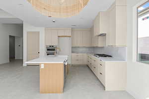Kitchen with cream cabinetry, a center island with sink, modern cabinets, light stone countertops, and recessed lighting