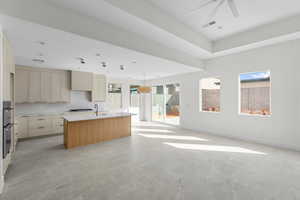 Kitchen with open floor plan, an island with sink, cream cabinetry, light stone counters, and decorative light fixtures