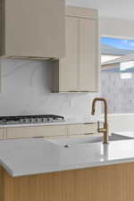 Kitchen with cream cabinets, stainless steel gas cooktop, decorative backsplash, exhaust hood, and light stone counters