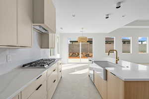 Kitchen featuring modern cabinets, wall chimney range hood, light stone countertops, stainless steel appliances, and pendant lighting