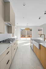Kitchen with modern cabinets, light stone countertops, stainless steel appliances, wall chimney range hood, and decorative light fixtures