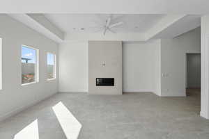 Unfurnished living room featuring a raised ceiling, a glass covered fireplace, and ceiling fan