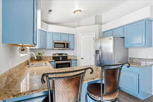 Kitchen with blue cabinets, stainless steel appliances, a kitchen breakfast bar, light stone counters, and vaulted ceiling