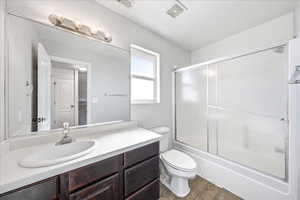 Bathroom with vanity, enclosed tub / shower combo, and dark wood-type flooring