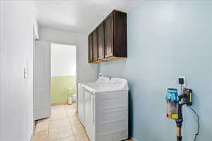 Washroom featuring cabinet space, light tile patterned floors, and separate washer and dryer
