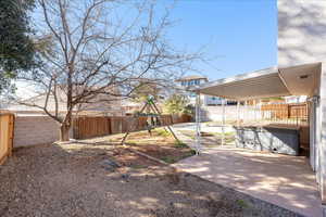 Fenced backyard with a hot tub, a playground, and a patio