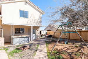 Rear view of house featuring a playground, a jacuzzi, stucco siding, and a fenced backyard