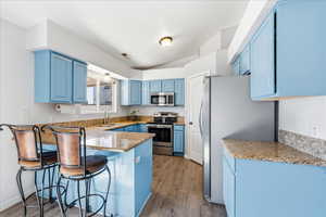 Kitchen featuring blue cabinetry, appliances with stainless steel finishes, light stone counters, a kitchen bar, and a peninsula