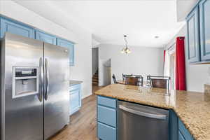 Kitchen featuring blue cabinetry, appliances with stainless steel finishes, pendant lighting, light wood finished floors, and light stone counters
