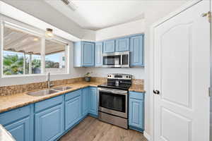 Kitchen featuring blue cabinets, appliances with stainless steel finishes, light wood finished floors, and light stone countertops