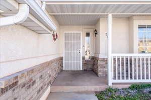 Entrance to property with covered porch, stucco siding, and stone siding