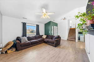 Living room featuring stairway, light wood finished floors, ceiling fan, and lofted ceiling