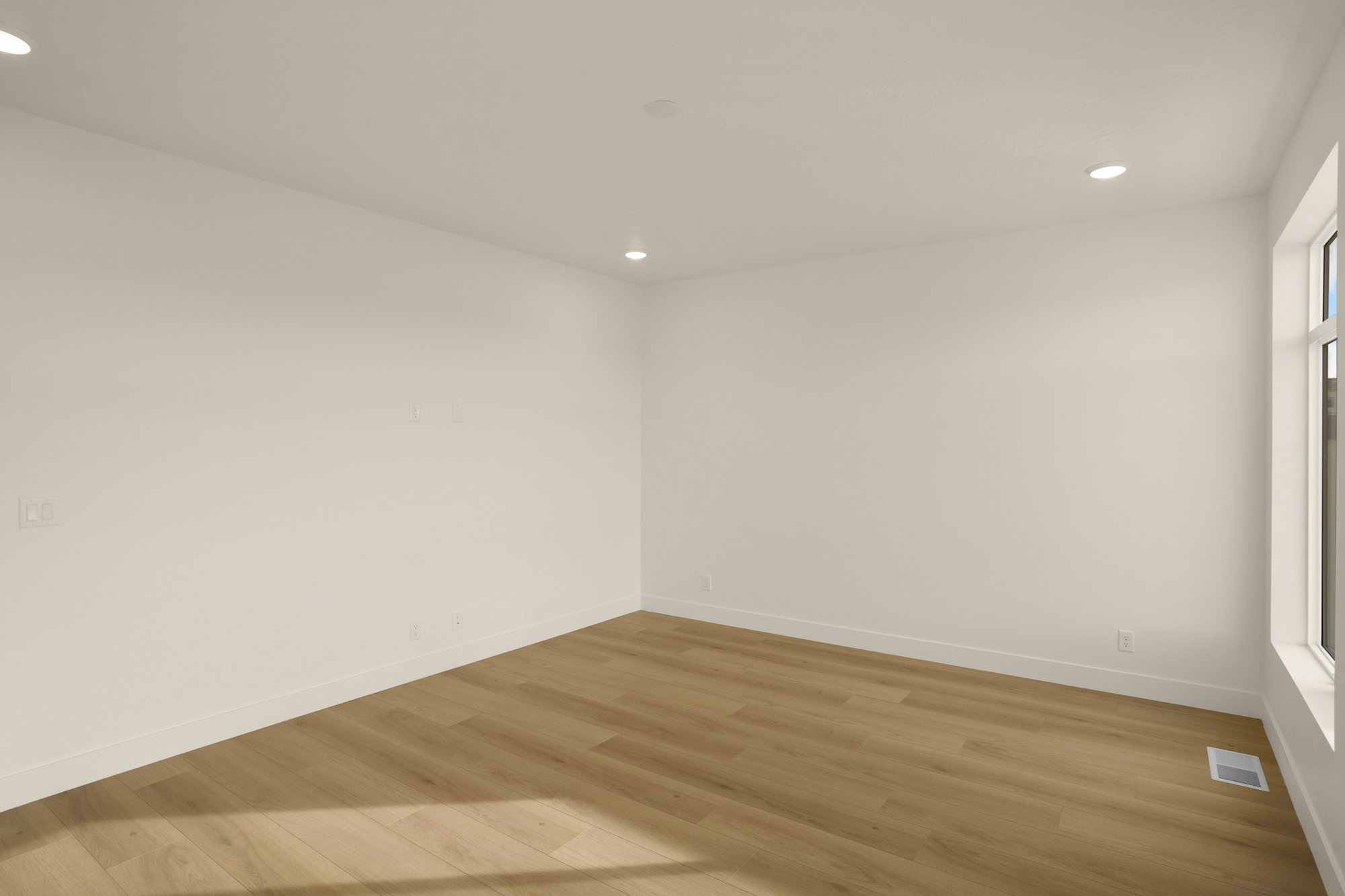 Spacious interior room featuring light wood-finish flooring, recessed lighting, white baseboards, and a large window providing ample natural light