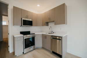 Kitchen with appliances with stainless steel finishes, modern cabinets, light wood-type flooring, and light stone countertops