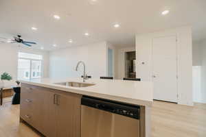 Kitchen featuring dishwasher, a center island with sink, recessed lighting, light wood-type flooring, and light stone counters