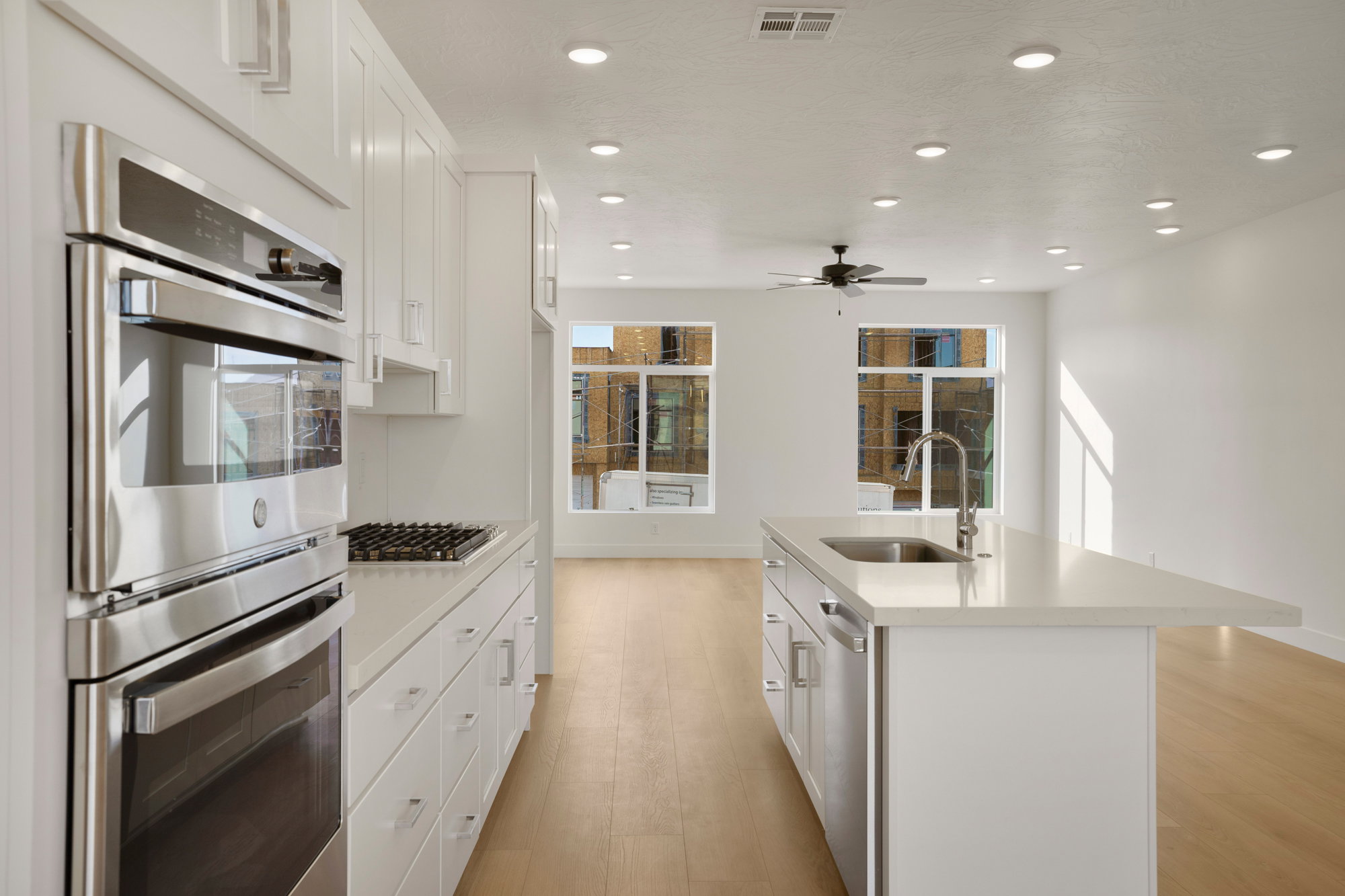 Open-concept kitchen featuring white shaker cabinetry, stainless steel double oven, gas cooktop, and an island with an undermount sink