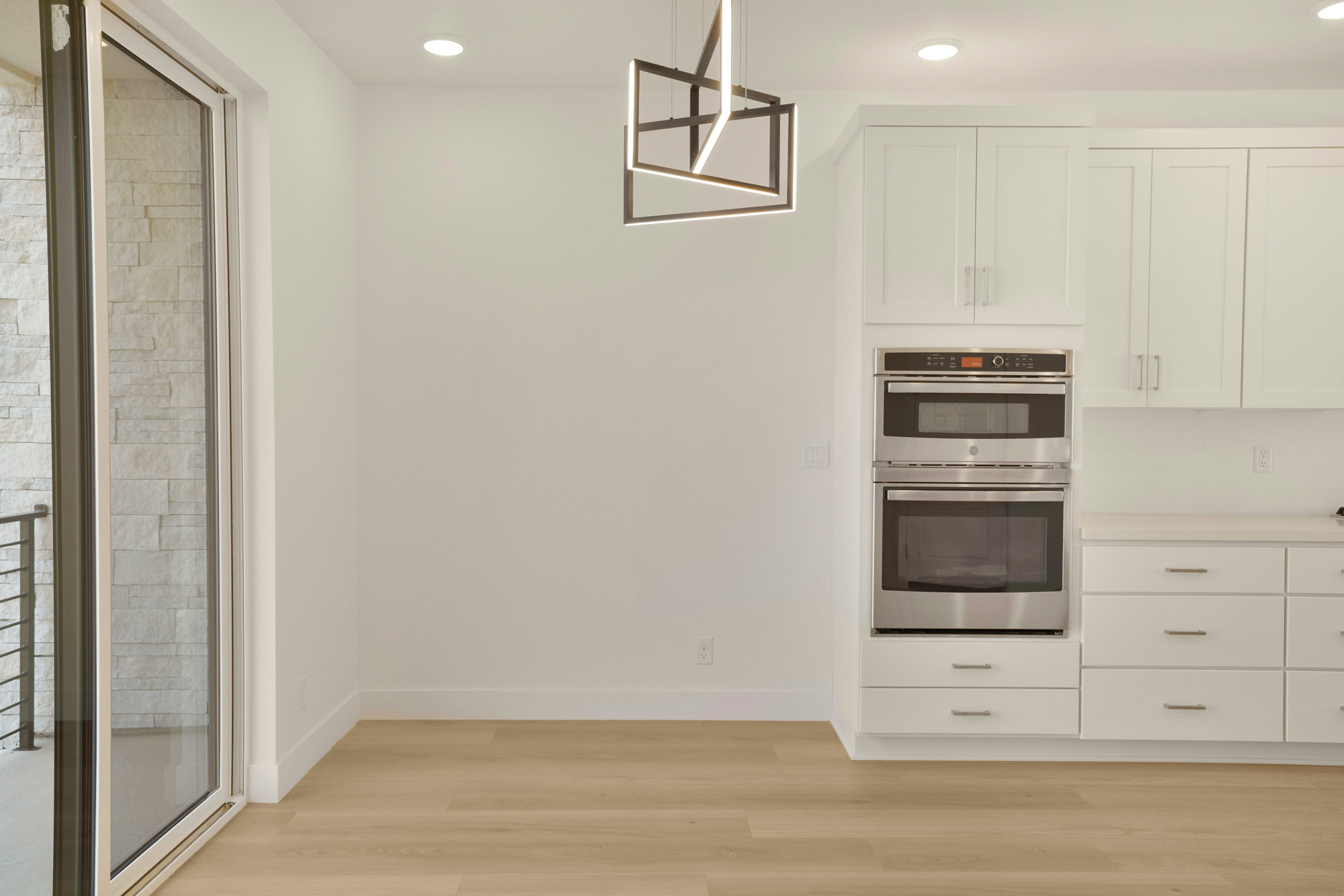 Contemporary kitchen area featuring stainless steel double ovens, white cabinetry, and light wood-finish flooring
