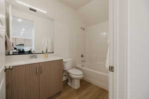 Full bathroom with vanity, tub / shower combination, light wood-style floors, and vaulted ceiling
