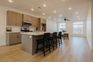 Kitchen with a center island with sink, a breakfast bar area, recessed lighting, modern cabinets, and appliances with stainless steel finishes