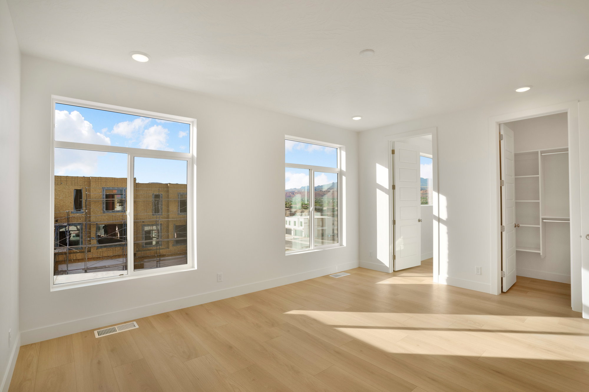 Spacious room featuring multiple large windows, wood-finish flooring, recessed lighting, and a built-in closet system