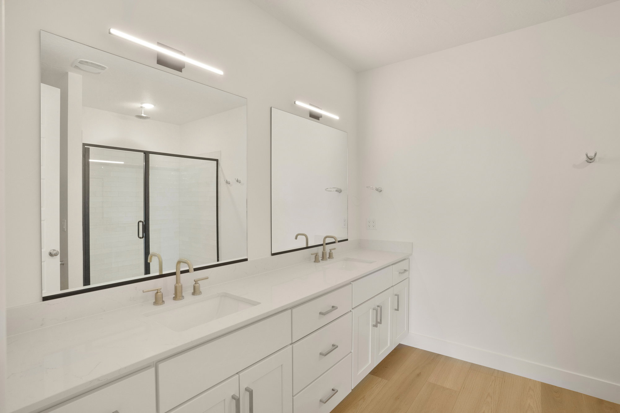 Dual vanity featuring white shaker-style cabinetry, white countertops, and brushed brass fixtures