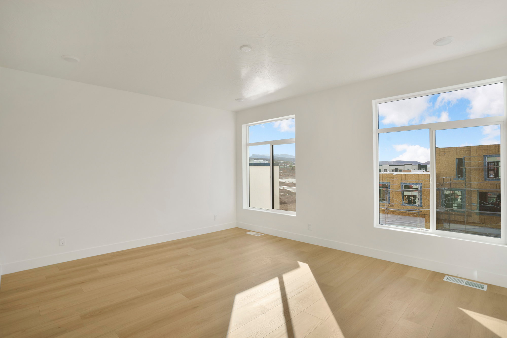 Spacious room featuring light wood-finish flooring, white baseboards, and crisp white walls