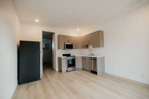 Kitchen with stainless steel appliances, modern cabinets, light wood finished floors, recessed lighting, and light brown cabinets