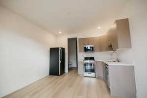 Kitchen featuring light countertops, stainless steel appliances, light wood-type flooring, modern cabinets, and recessed lighting