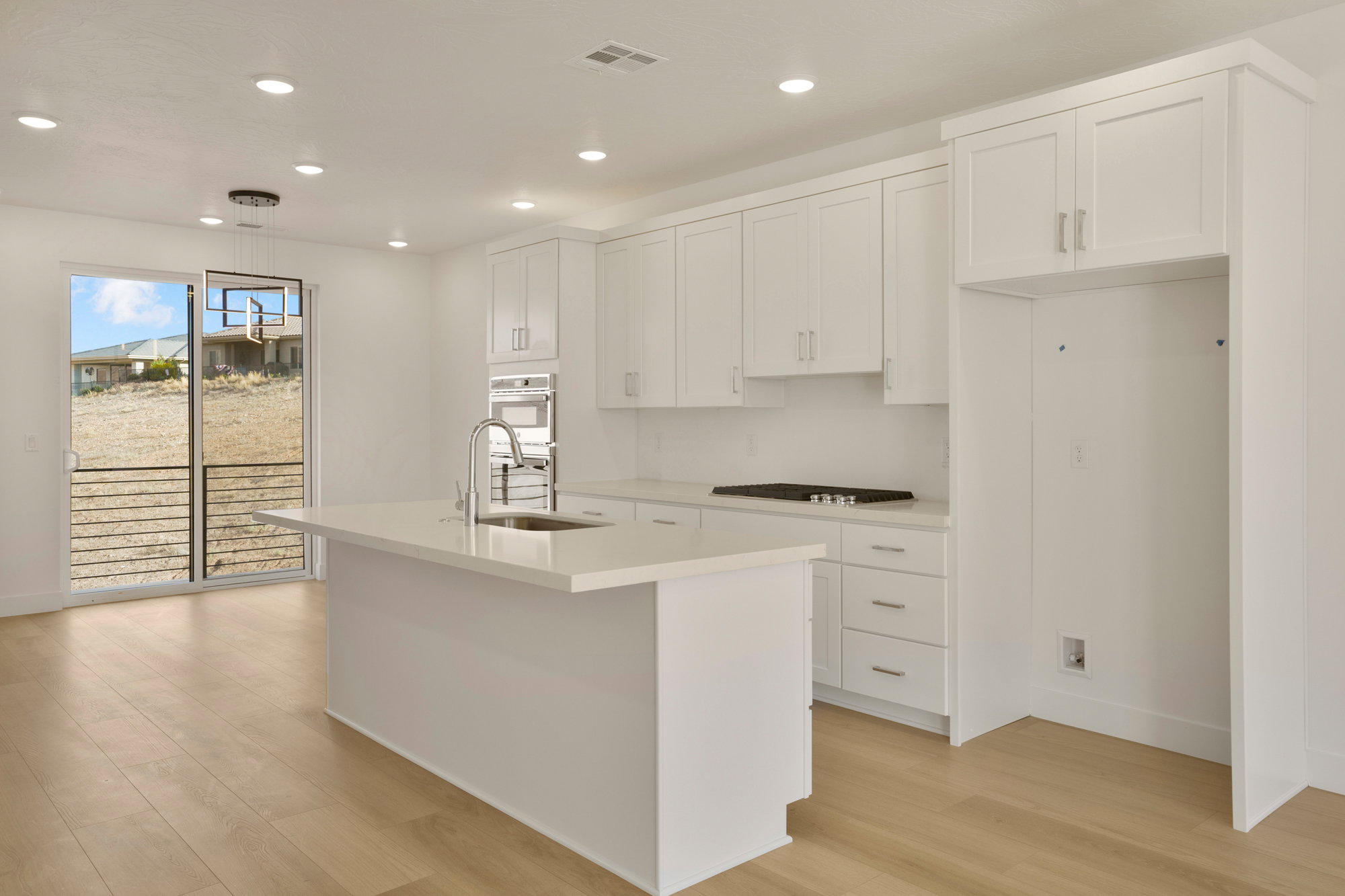 Bright kitchen featuring white shaker cabinetry, an island with an integrated sink, a built-in oven, a cooktop, and wood-finish flooring