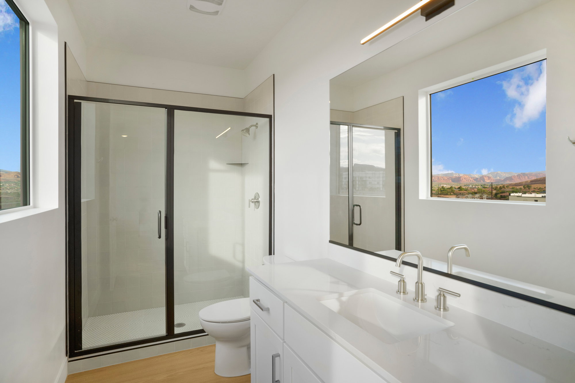 Contemporary bathroom featuring a spacious glass-enclosed shower with black trim, a large vanity with an integrated sink, and an expansive mirror