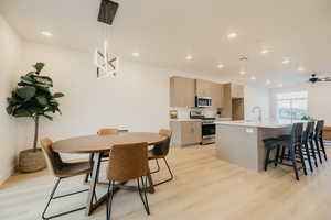 Kitchen featuring stainless steel appliances, a breakfast bar, pendant lighting, light wood-style floors, and a kitchen island with sink