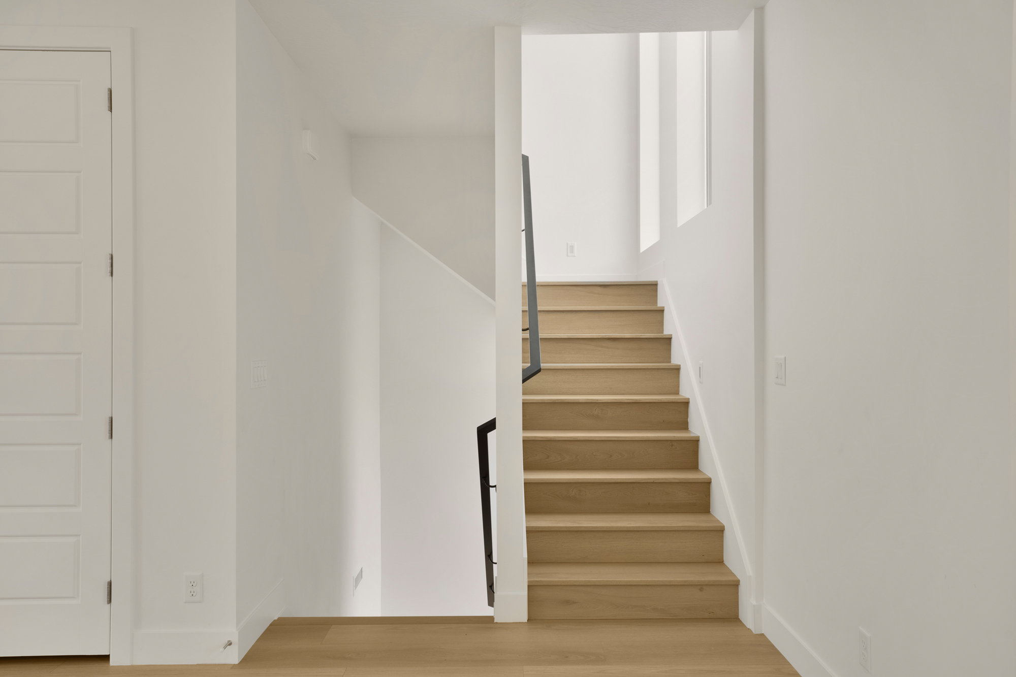 Staircase featuring wood-finish treads and risers, a contemporary black metal railing, crisp white walls, and wood-finish flooring