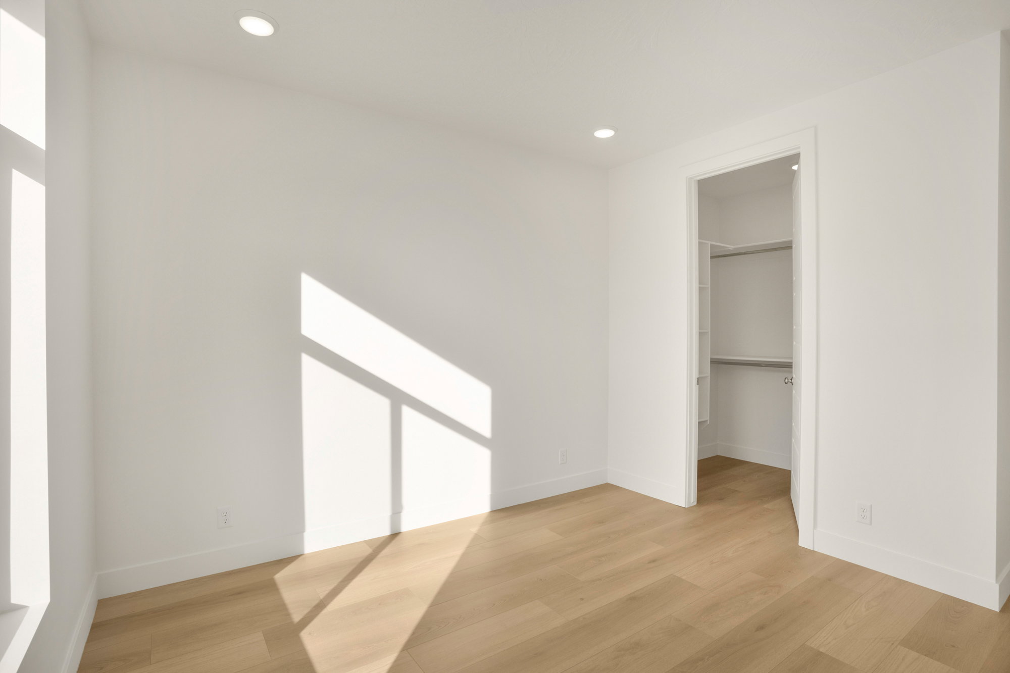 Bright interior space featuring wood-finish flooring, recessed ceiling lighting, a tall window, and a walk-in closet with built-in shelving and hanging rods