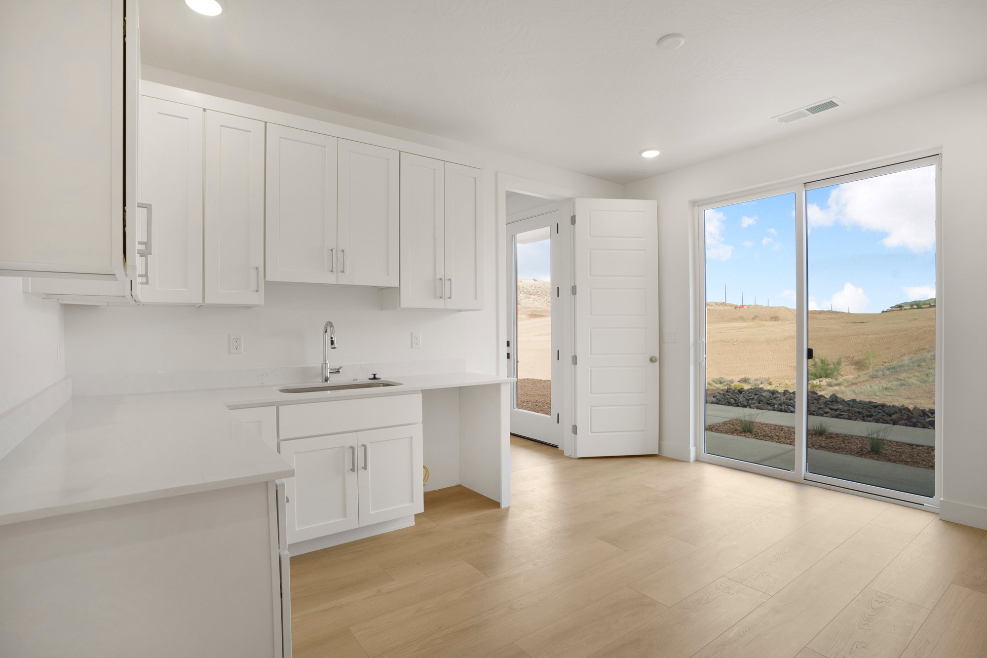Contemporary space featuring wood-finish flooring, white cabinetry, a stainless steel sink with a gooseneck faucet, and white countertops