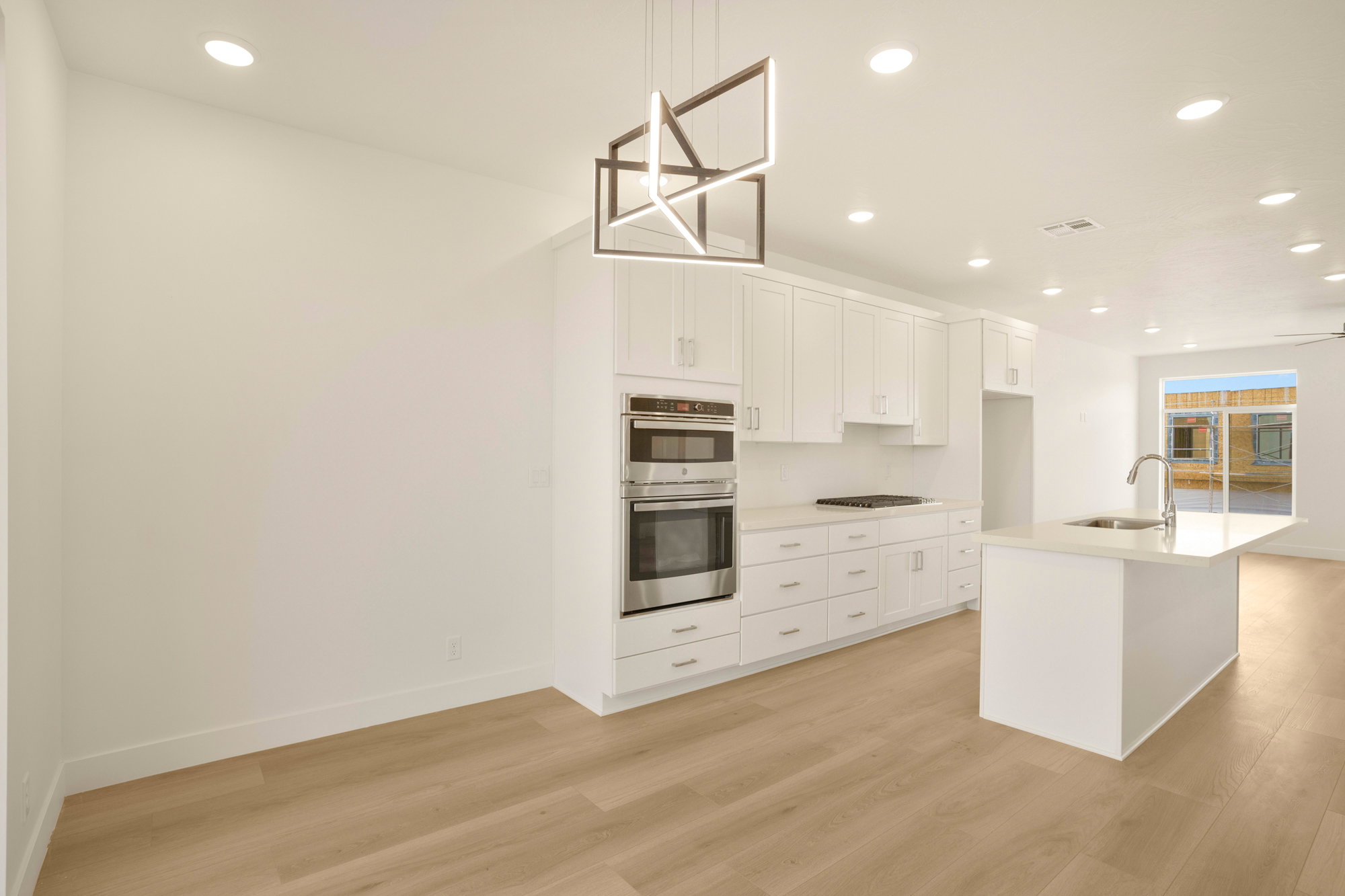 Contemporary kitchen featuring white cabinetry, stainless steel double oven, gas cooktop, white countertops, and a central island with an integrated sink