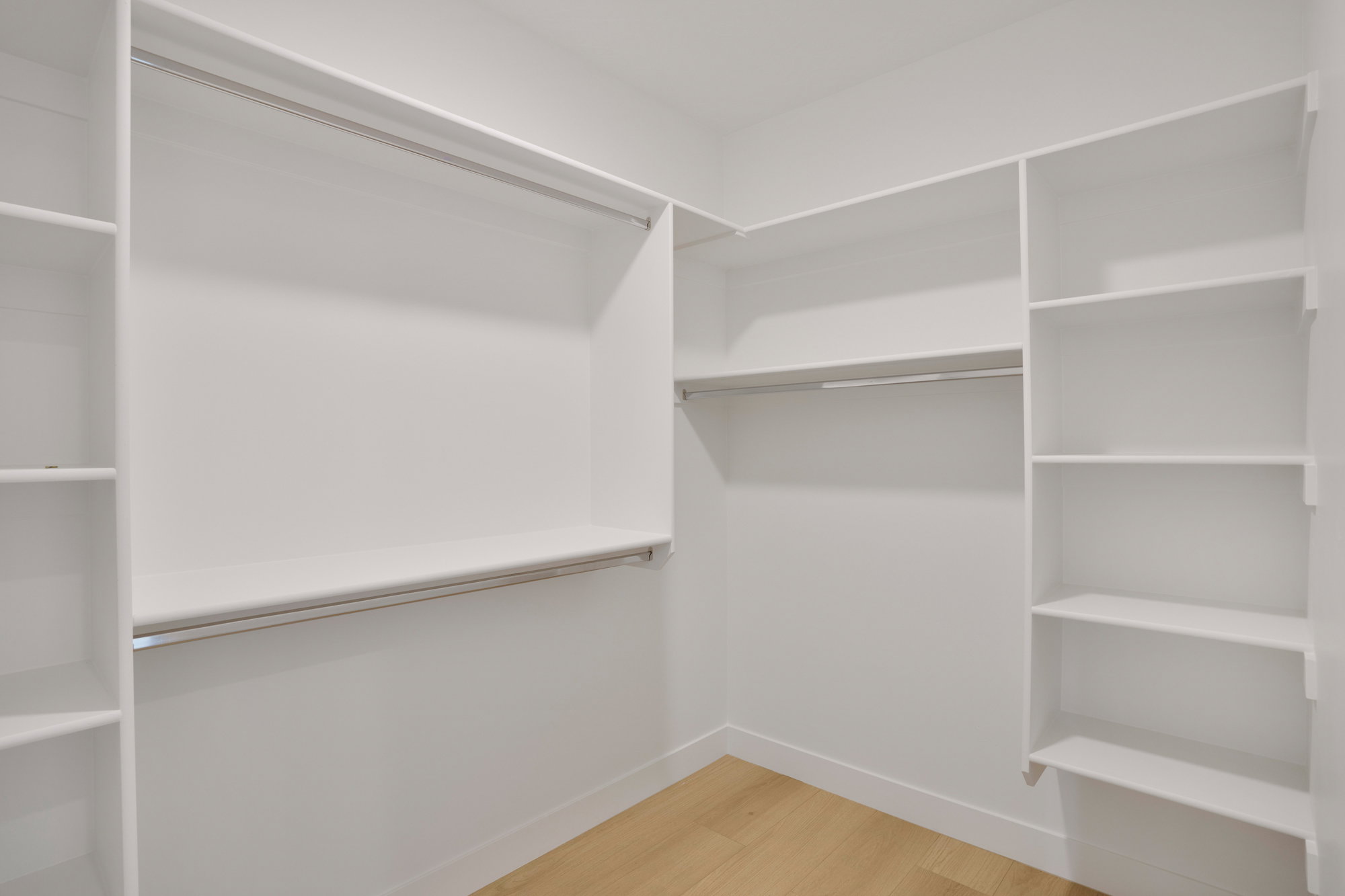 Walk-in closet featuring light wood-finish flooring, white built-in shelving, white walls, and chrome hanging rods
