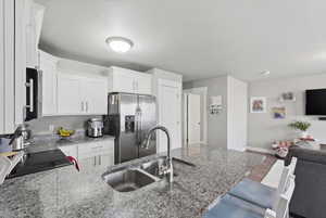 Kitchen featuring appliances with stainless steel finishes, light stone countertops, white cabinetry, and open floor plan