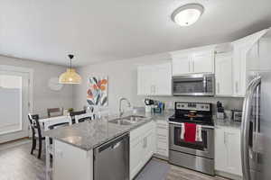 Kitchen with appliances with stainless steel finishes, a peninsula, a breakfast bar area, light stone counters, and pendant lighting