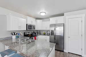 Kitchen with stainless steel appliances, white cabinets, a peninsula, light stone countertops, and a breakfast bar