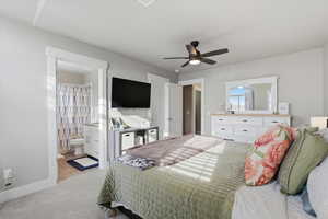 Bedroom with light colored carpet, ceiling fan, and connected bathroom